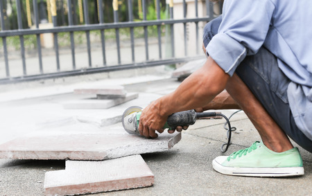 Grinder worker cuts a stone tile with electric toolの写真素材