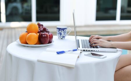 Business people working on laptop computer with plate of fresh fruit by swimming pool