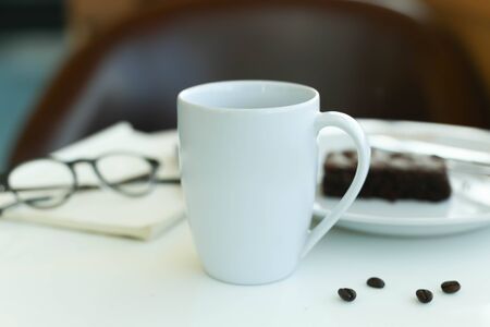 Coffee with blank paper note and glasses and chocolate brownie on white tableの写真素材