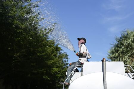 Unidentified man on water truck watering big tree in the parkの写真素材