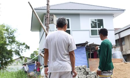 Unidentified man discussion plans workers pointing at house under construction siteの写真素材