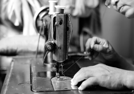 Woman hand threading needle into sewing machine needle in black and whiteの写真素材