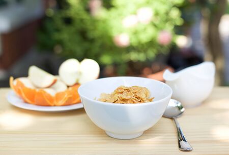 Bowl of honey-sugar corn flakes and spoon and slice of fruitの写真素材