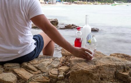 Man relaxing sitting on the rock having a drink on the beach on vacationの写真素材