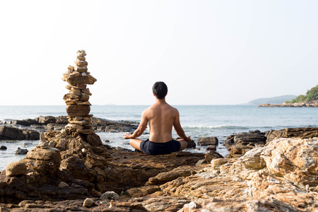 Unidentified man practice yoga on the rock by the oceanの写真素材