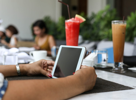 women hands with tablet computer and fruit shake on the table at lunchの写真素材