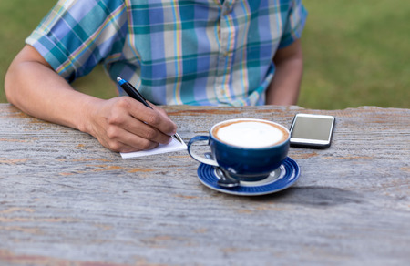 Bussinessman writting something on paper with  coffee cup and cell phone on the tableの写真素材