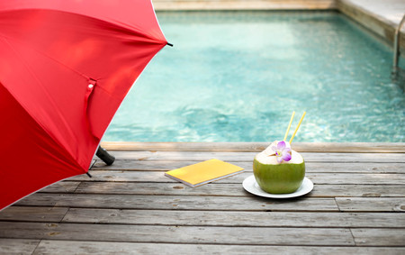 Coconut juice with flower and book and red umbrella by the swimming poolの写真素材