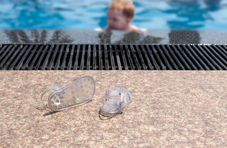 Baby flip flops on the swimming pool floor with baby blurred on backgroundの写真素材