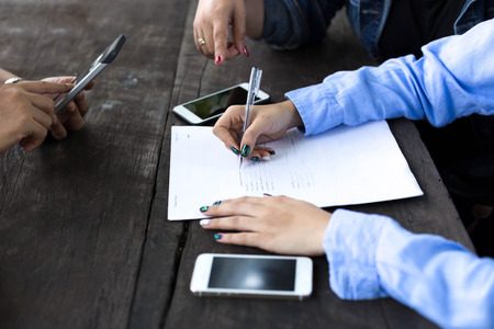 Business woman's hand with pen completing application form on wooden table