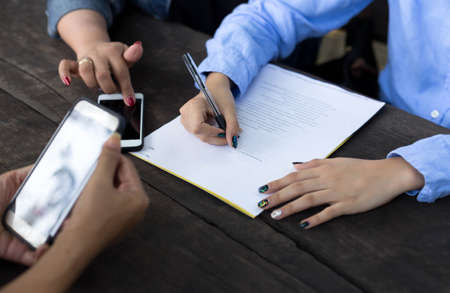 Business woman's hand with pen completing application form on wooden tableの写真素材