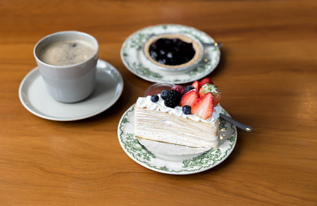 Crape cake with strawberry jam and cherry fruit on dish with coffee on the table