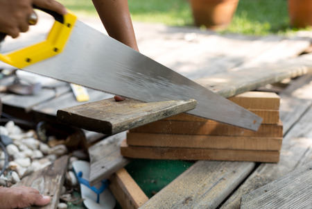 Carpenter fixing decking by sawing a wood with hand wood sawの写真素材