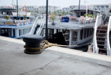 Mooring rope with a knotted tied around a cleat with tour boat at the pierの写真素材