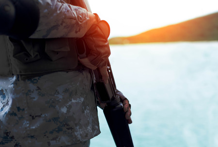 Selected focus Navy hand holding rifle standing on guard in sunlight with ocean in background