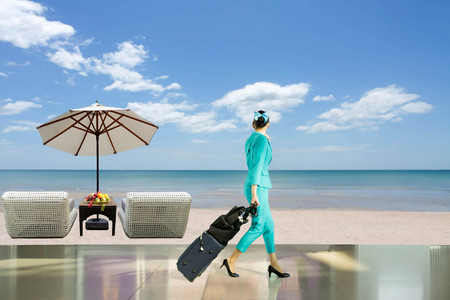 Travel vacation concept woman flight attendant with suitcase and beach chair with fresh fruit and umbrella on the beachの写真素材