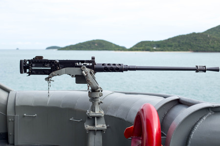 Machine gun on the side of Thai Navy warship with island and ocean as backgroundの写真素材