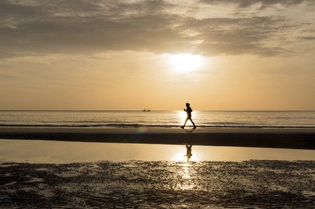 silhouette of woman doing a brisk walking on the beach at sunset-sunriseの写真素材