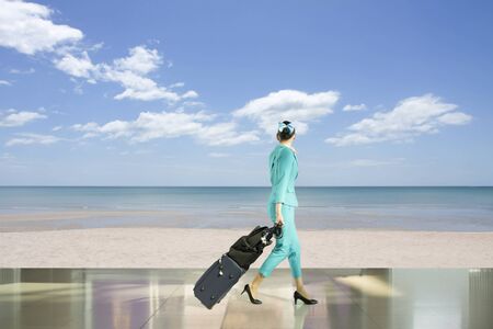 Travel concept flight attendant walking on the beach with suitcaseの写真素材