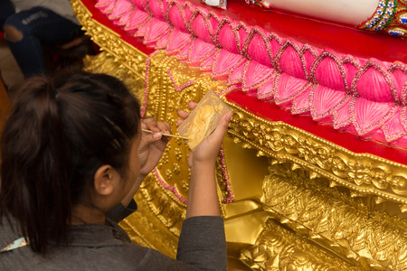 Woman painting buddha statue in gold color with small paint brushの写真素材