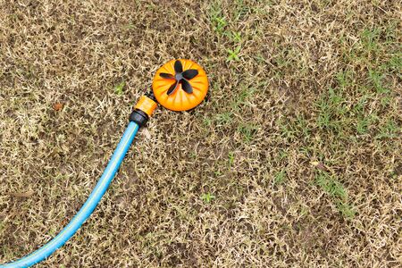 Orange sprinkler in dry grass in the gardenの写真素材