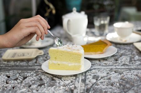 Woman holding spoon eating coconut cake with cup of tea on vintage metal table at tea timeの写真素材