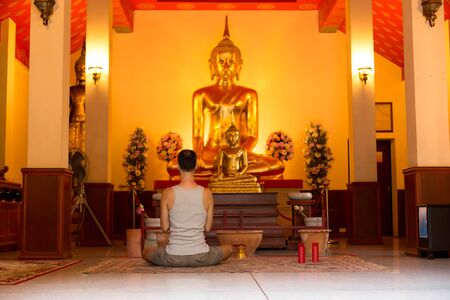 Man meditating in front of buddha statue in templeのeditorial素材