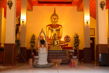 Man doing Yoga meditating in front of buddha statue in templeのeditorial素材