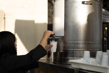 Woman filling plastic cup at water cooler with nature sunlightの写真素材