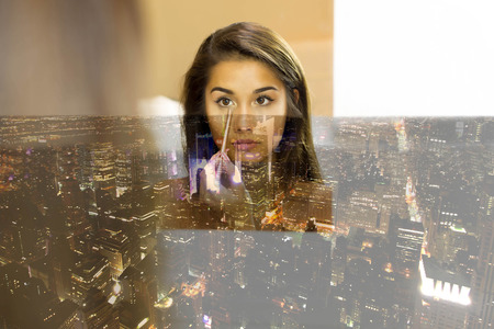 Reflective mixed race young woman applying eyeshadow with brush looking in the mirrorの写真素材