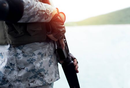 Selected focus Navy hand holding rifle standing on guard in sunlight with ocean in backgroundの写真素材