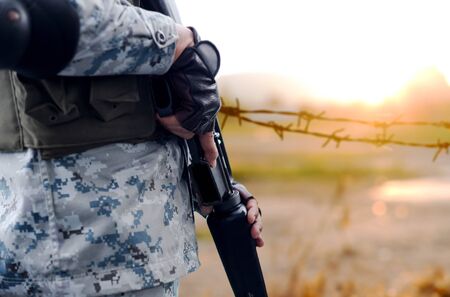 Selected focus army with rifle gun with blurred background wire fence in sunsetの写真素材