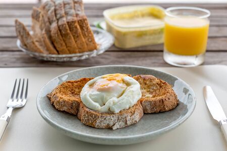 Breakfast fried eggs on crusty toasted bread with orange juice and butter in backgroundの写真素材
