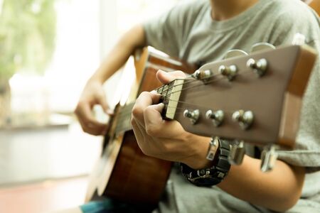 Asian teenager playing the acoustic guitar indoors