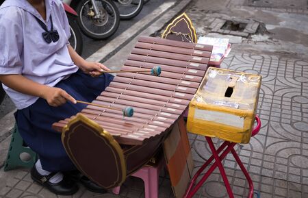 Young student with uniform play drum sticks striking the xylophone on the street for school donation