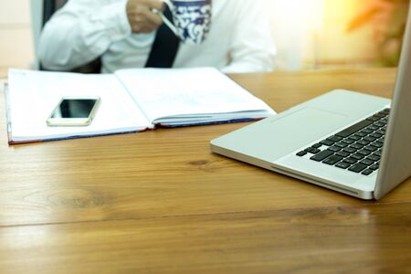 Selected focus on keyboard businessman relaxing while drinking a mug of coffee with computer notebook on the wooden table with light flareの写真素材
