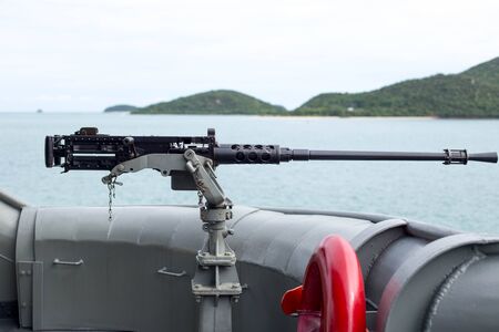 Machine gun on the side of Thai Navy warship with island and ocean as backgroundの写真素材