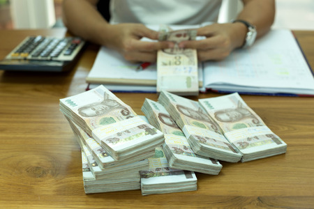Finances Businessman counting Thai money with calculator on the side and notebookの写真素材