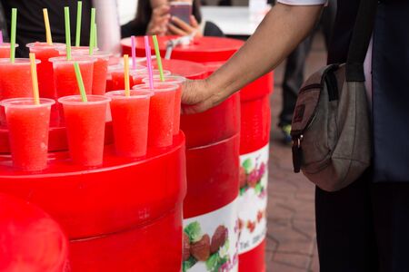 Refreshing red colorful, fruity drinks woman hand pick up taking drink from plastic glassの写真素材