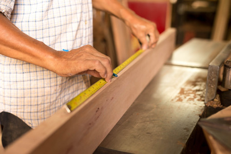 Selected focus carpenter hand measuring tape on wood plank in work placeの写真素材