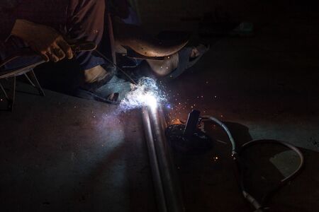 Man with protective mask welding metal in dark contrast backgroundの写真素材