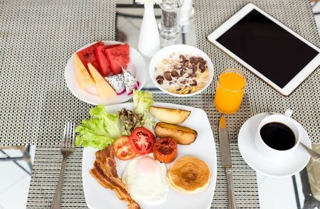 Breakfast set on the table with pancakes, bacon, eggs and coffee top view  with ipadの写真素材