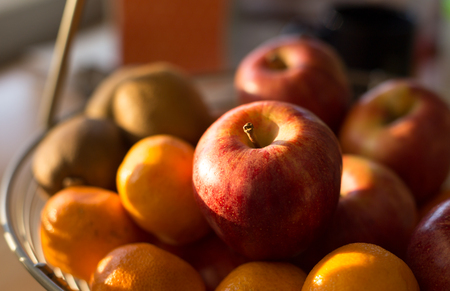 Ripe apple fruit in basket on wooden table illuminated by afternoon sunlightの写真素材