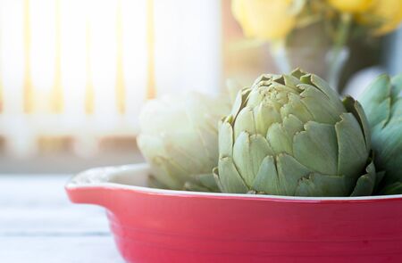 Fresh organic green artichokes in red blow on the table in sunlightの写真素材