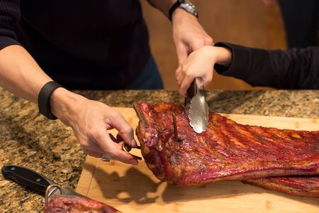 Father and son hand holding spare ribs on wooden board on family dinner timeの写真素材