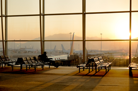 Passenger sitting in a lobby airport waiting for flight using cell phone in silhouetteの写真素材