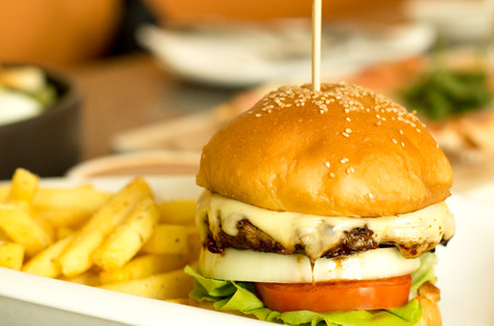 Hamburger with melted cheese and vegetable and chips in backgroundの写真素材