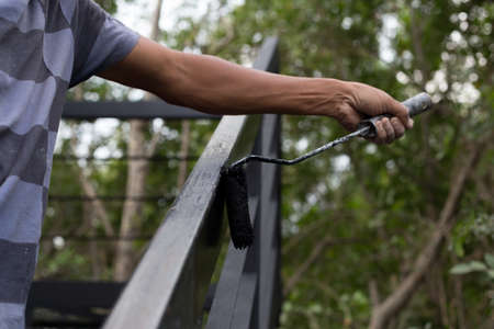 Hand holding paint roller applying black paint on metal stair outsideの写真素材