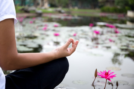 Woman doing yoga meditation next to lotus pond outdoorsの写真素材