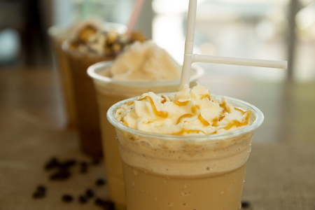 Iced caramel coffee frappe with whipped cream in plastic glass in blur backgroundの写真素材